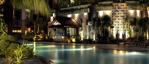 A pool area with a traditional-style building, a stone wall with decorative patterns, and lush greenery. - Hotel Kristal (Jakarta)