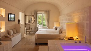 A bedroom with a large bed, a sitting area, a bathtub, and a view of the outdoors. - Masseria San Francesco (Fasano)