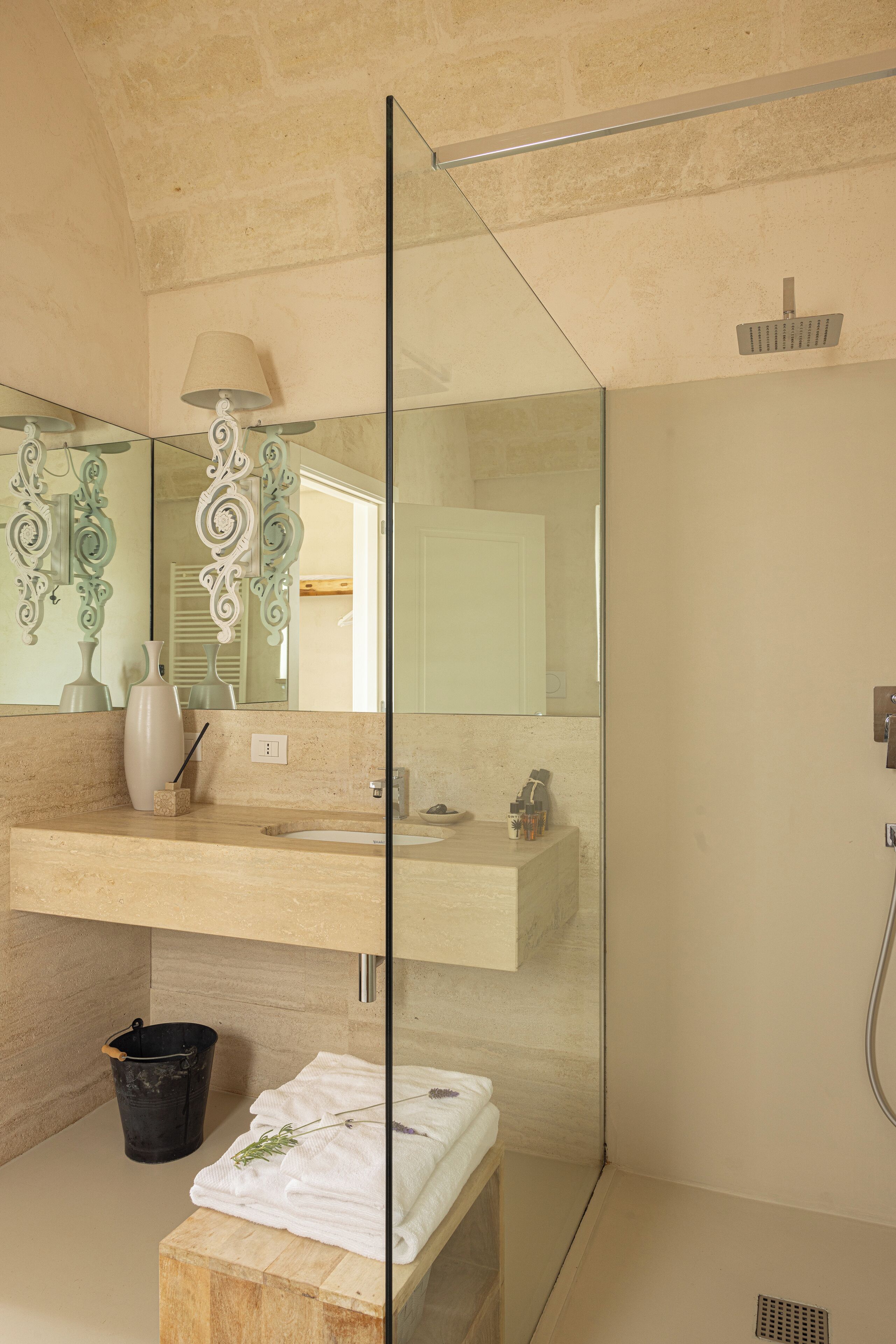 Un baño moderno con ducha envuelta en vidrio, tocador con espejo y banco de madera.