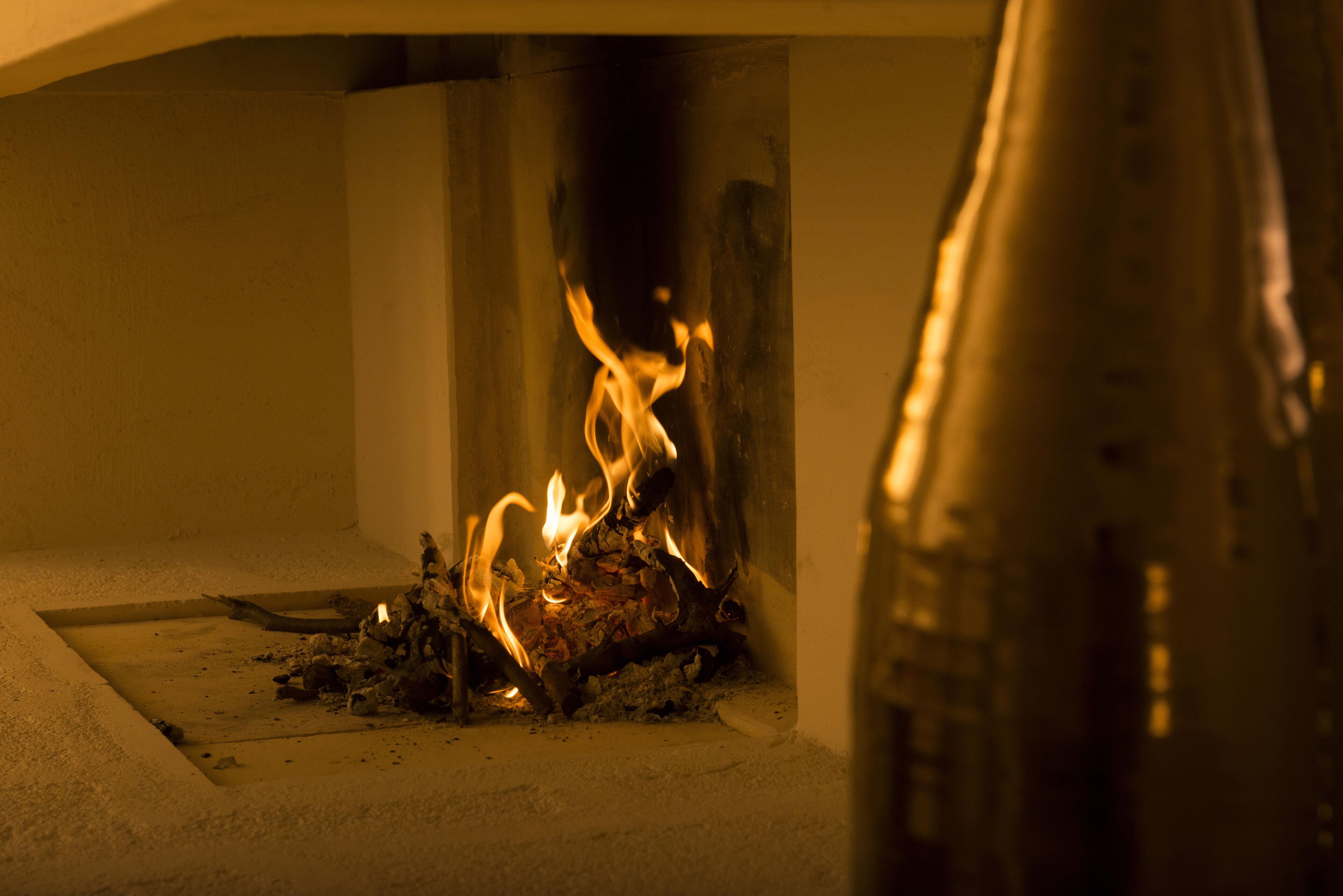 Una chimenea con leña ardiendo y una botella metálica cerca.