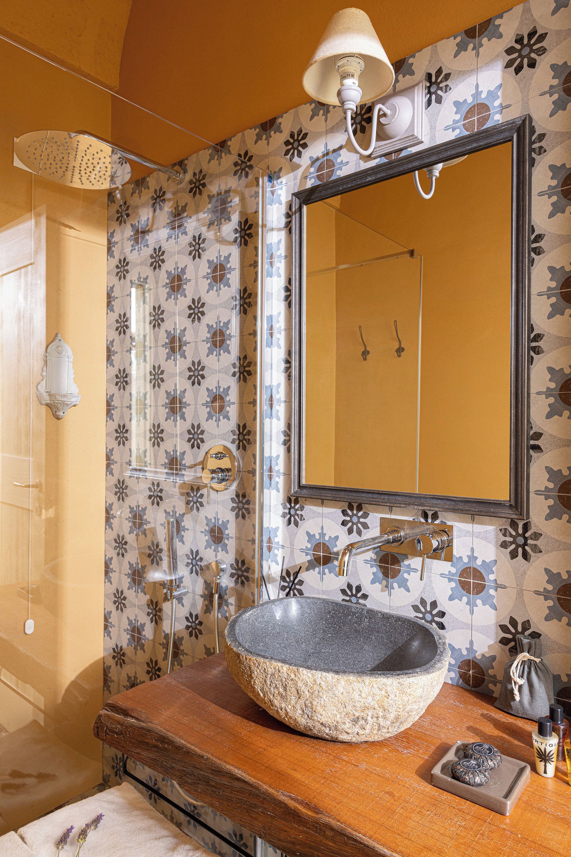Un baño con un lavamanos de piedra, un espejo grande y azulejos estampados.
