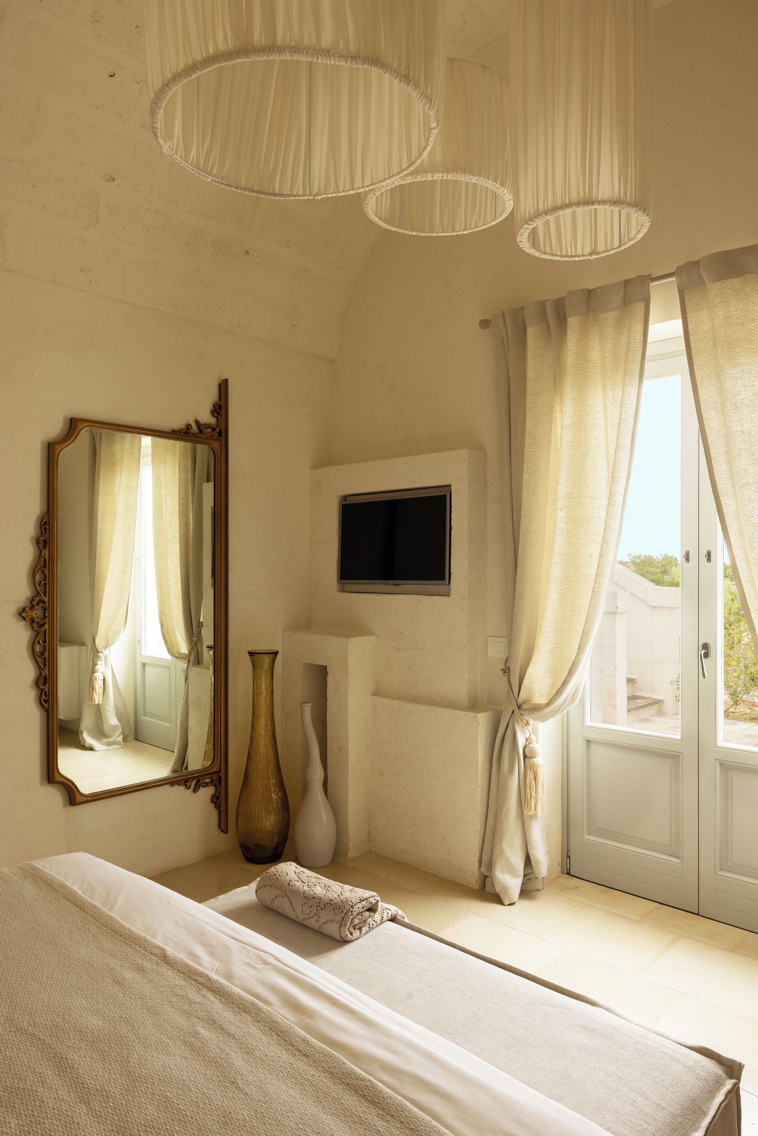 Un dormitorio con cama, espejo, televisor y ventana con cortinas.