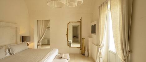 A bedroom with a large bed, a mirror, a vase, and curtains.