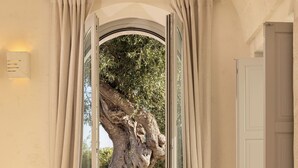 A bedroom with a large window, a bed, a wicker basket, and a white door. - Masseria San Francesco (Fasano)