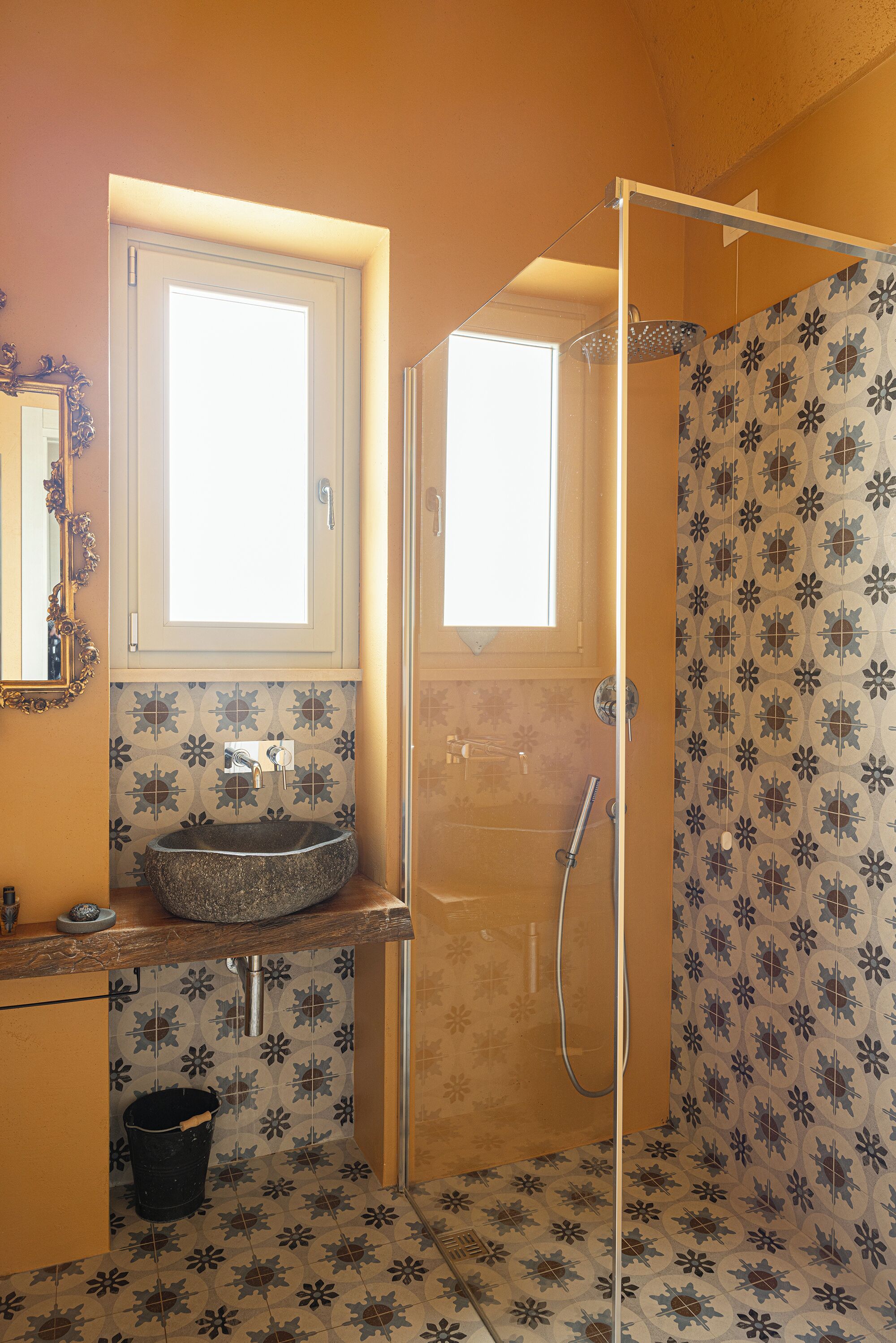 Un bagno con un lavabo tondo, uno specchio, una doccia con porta in vetro e piastrelle decorate.