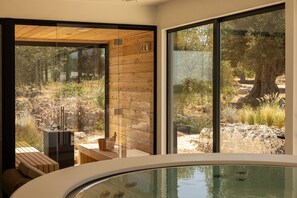Et moderne spaområde med jacuzzi, træsiddepladser og udsigt over et naturlandskab gennem store vinduer.