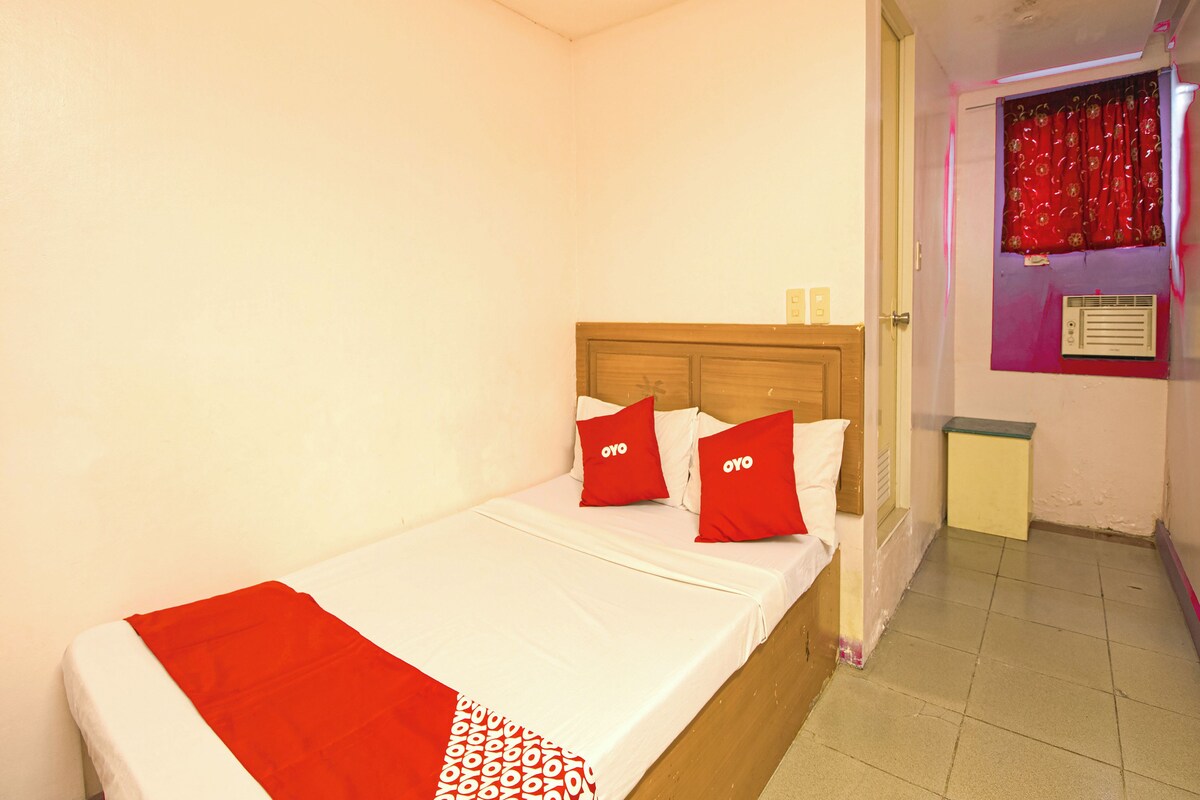 A single bed with a wooden headboard, white bedding, and red pillows with "OYO" branding.