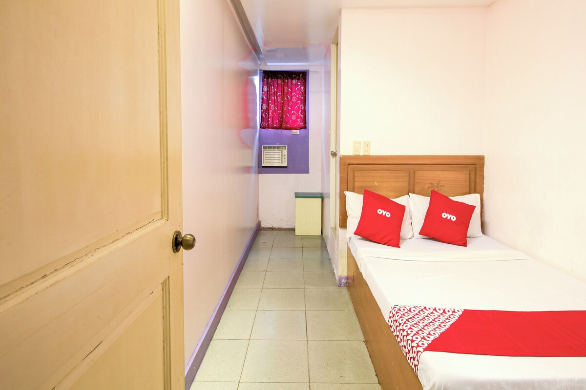 A hotel room with a bed, a wooden headboard, and a window with pink curtains.