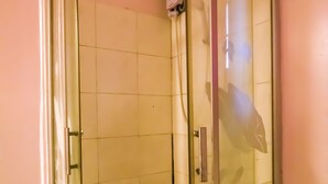 A glass-enclosed shower stall with a white tiled floor and a handheld showerhead. - OYO 790 Mango Inn (Manila)