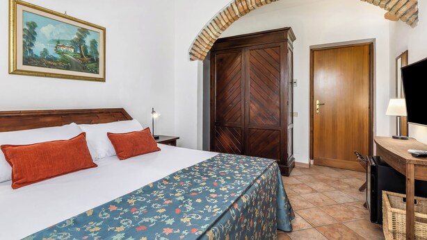 Una habitación de hotel con una cama, un armario de madera, un escritorio con lámpara y un cuadro en la pared.