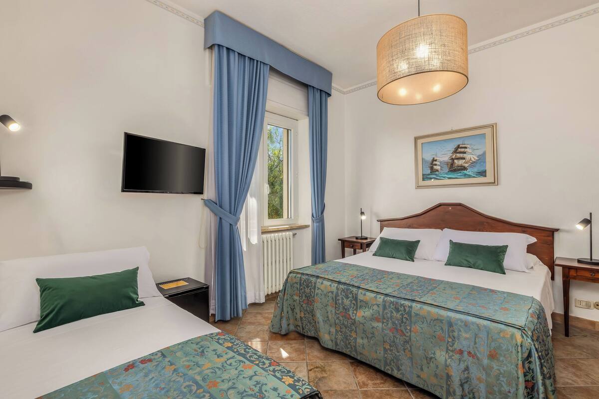 A hotel room with two beds, a television, a painting, and a window with curtains.