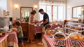 Una familia cenando en un salón con mesas a cuadros, un bufé con diferentes platos y una máquina de café.