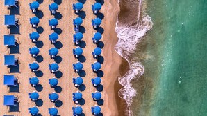 Vista aérea de una playa con hileras de sombrillas azules y sillas de playa.