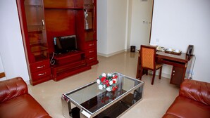 A living room with a glass coffee table, red leather sofas, a wooden entertainment center, and a desk with a telephone and cup.