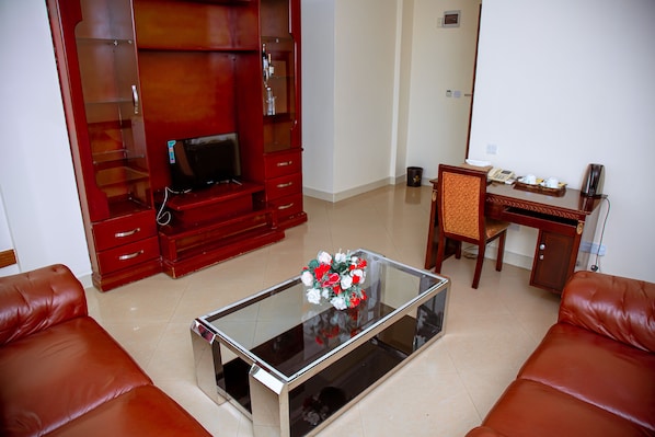 A living room with a glass coffee table, red leather sofas, a wooden entertainment center, and a desk with a telephone and cup.