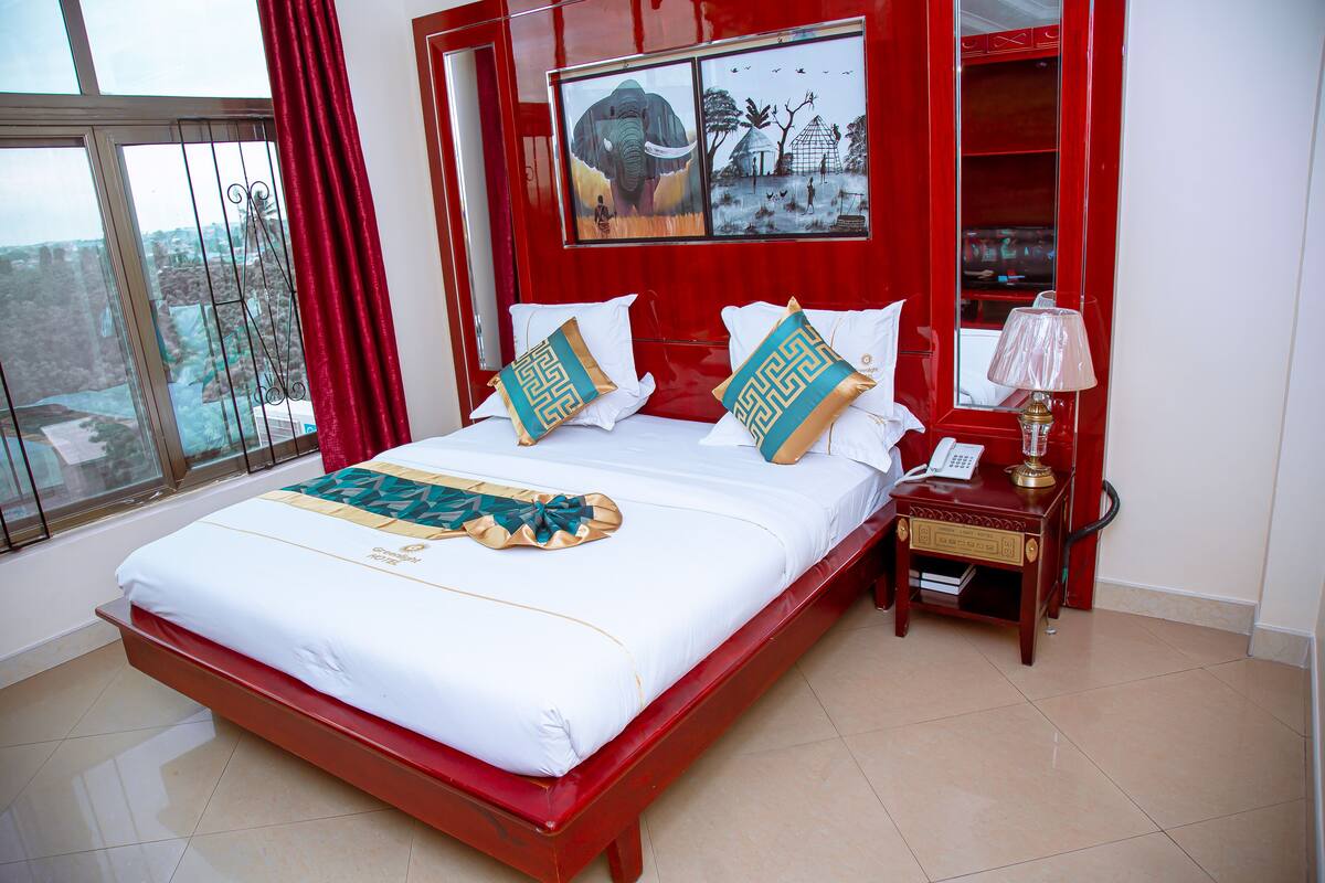 A hotel room with a large bed, a nightstand, a lamp, and a painting of an elephant.