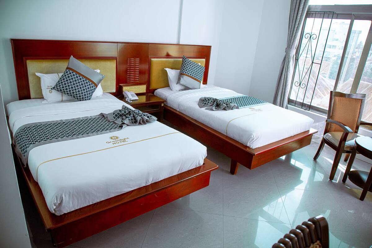 A hotel room with two beds, a wooden headboard, a small table, and a chair.