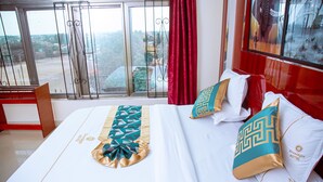 A hotel room with a large bed, red curtains, and a view of a cityscape through the window.