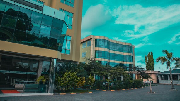 A modern building with large glass windows and a curved facade, surrounded by greenery and a paved courtyard.