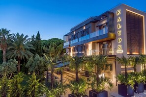 A modern hotel with a prominent balcony, multiple floors, and lush greenery surrounding the building.