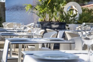 Outdoor dining tables with chairs, some with wine glasses on them, and potted plants in the background. - Kalyon Çeşme (Cesme)