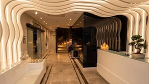 A modern hotel lobby with a wavy ceiling design, a reception desk, and a staircase leading to the upper floors. - Kalyon Çeşme (Cesme)