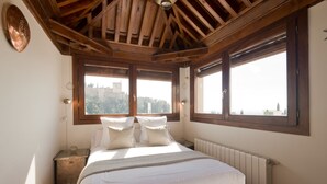 A bedroom with a wooden ceiling, large windows, a bed with white linens, and a radiator. - Casa Bombo (Granada)