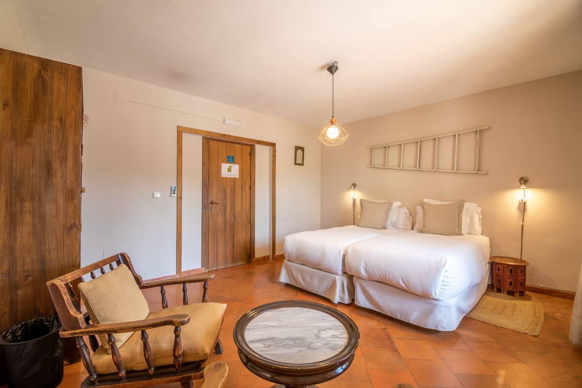 A bedroom with a large bed, a wooden chair, a round table, and a wooden wardrobe.