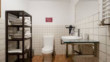 Een badkamer met een toilet, een plank met handdoeken, een wastafel en een bordje aan de muur.