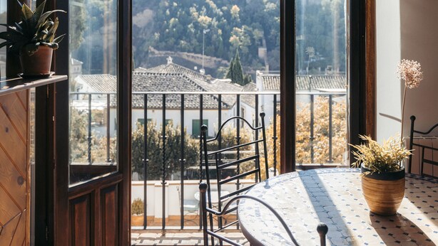 A balcony with a table and chairs, a potted plant, and a view of a cityscape. - Casa Bombo (Granada)