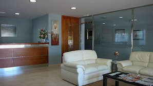 Una moderna recepción con un escritorio de madera, dos sofás de cuero blanco, una mesa de centro y un separador de vidrio.
