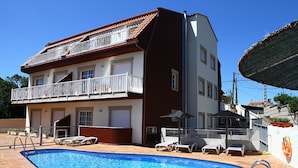 Un edificio de dos pisos con piscina, mobiliario exterior y un balcón.