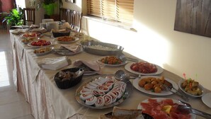 A buffet table with various dishes, including meats, cheeses, and bread, set up in a room with a window and plants in the background. - Hotel Giardino San Michele (Novi Velia)