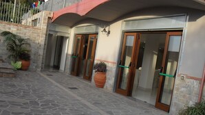 A building with a stone-paved entrance, large glass doors, and a red awning. - Hotel Giardino San Michele (Novi Velia)