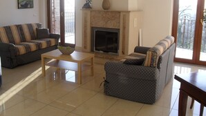 A living room with a fireplace, two sofas, a coffee table, and a door leading to a balcony. - Hotel Giardino San Michele (Novi Velia)