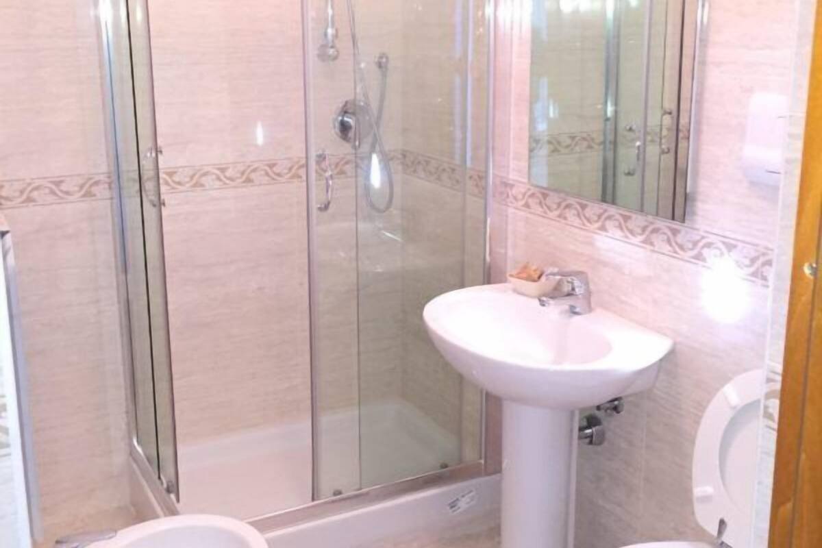 Une salle de bain avec une douche à parois de verre, un lavabo sur colonne et des toilettes.
