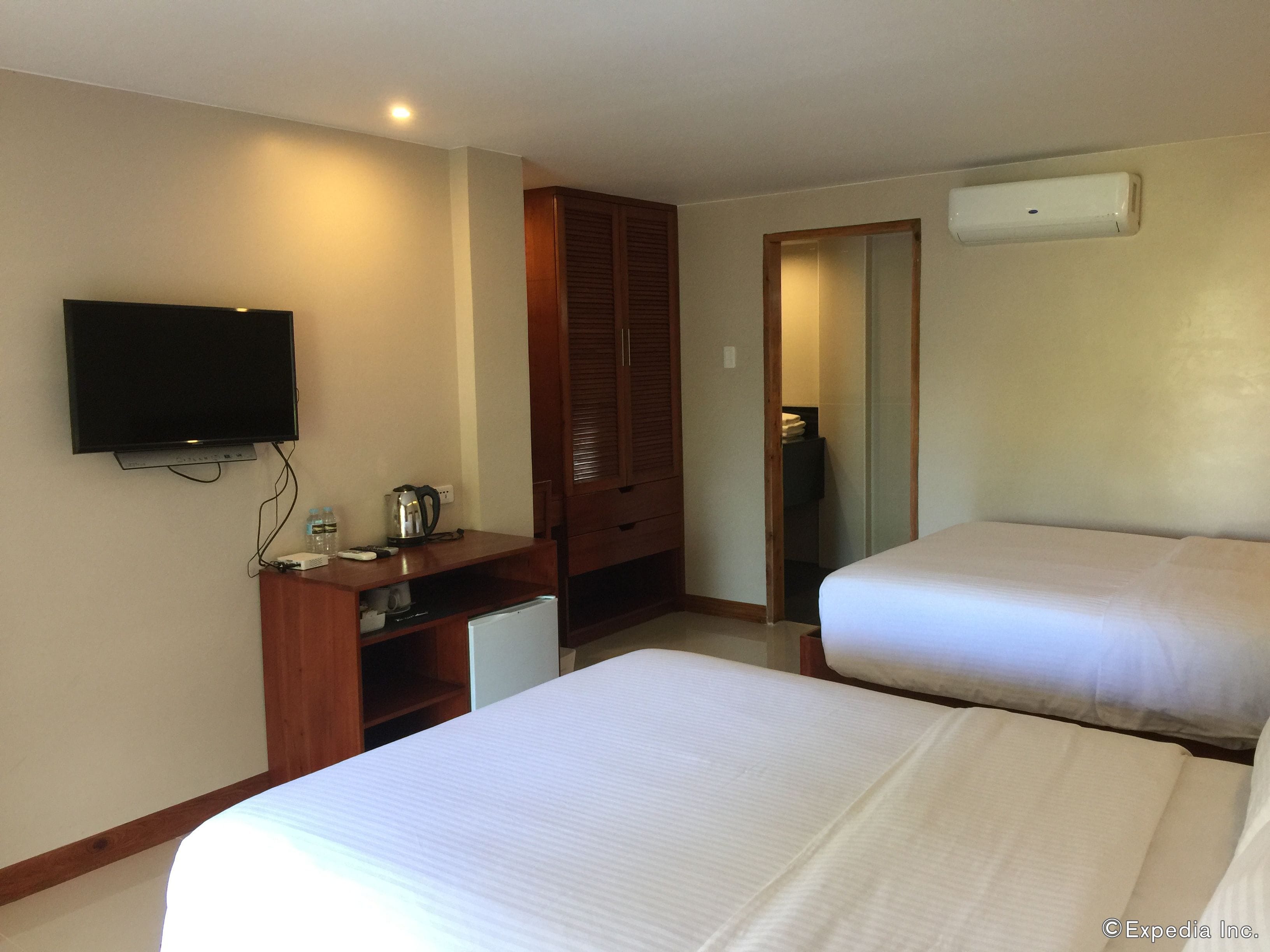 A hotel room with a TV, a desk with a kettle, a mini-fridge, and two beds.