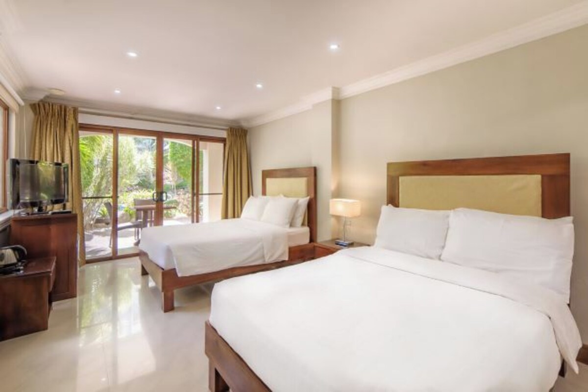 A hotel room with two beds, a desk with a chair, a TV, and a sliding glass door leading to an outdoor area.