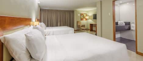 Habitación de hotel con dos camas, un escritorio, una silla, una lámpara y un baño visible a través de una puerta abierta.