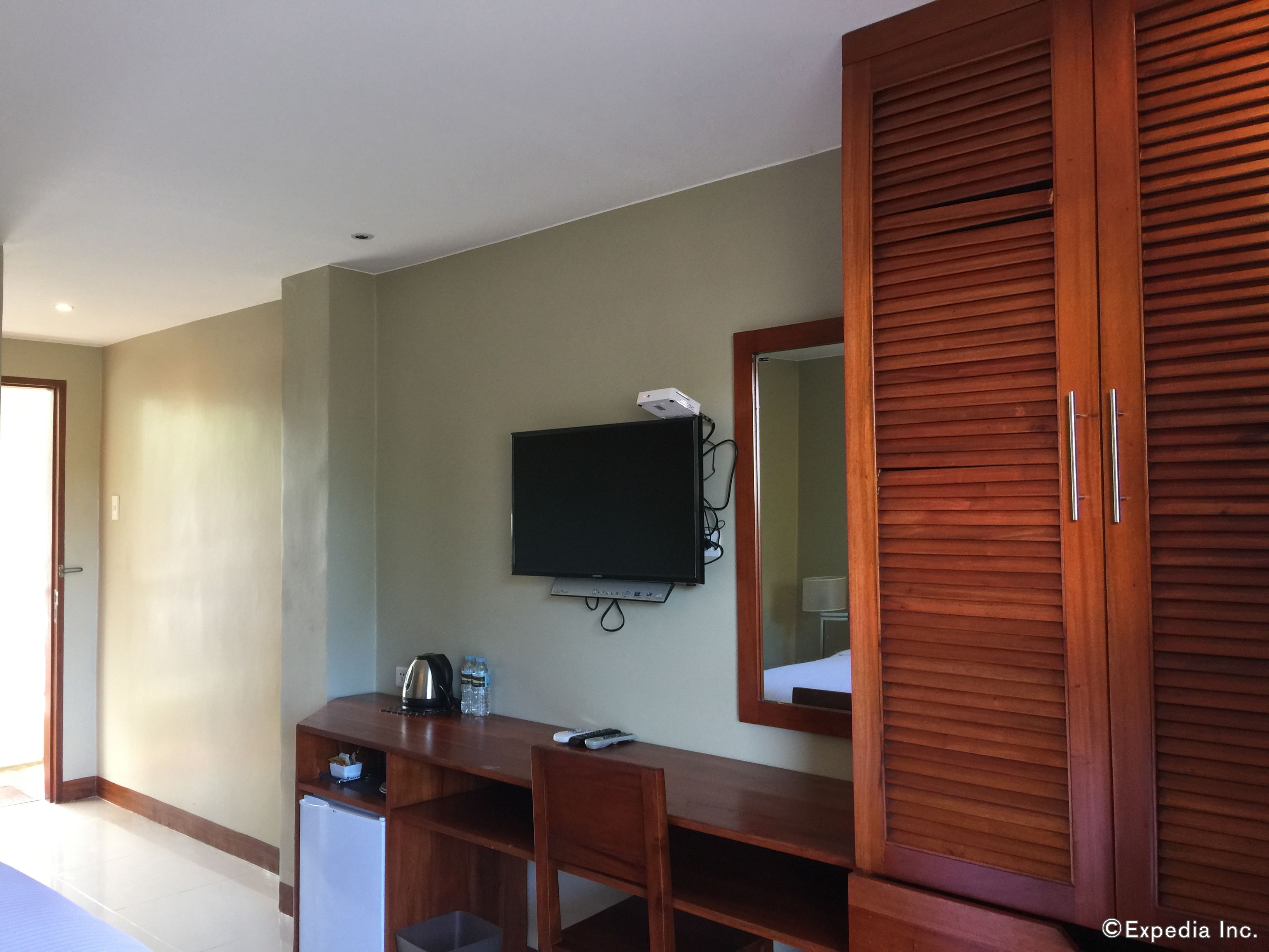 Una habitación de hotel con un escritorio de madera, un televisor montado en la pared, un espejo y un armario.