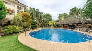 A swimming pool with a pebble border, surrounded by lush greenery and a thatched-roof structure. - Golden Palm Resort (Panglao)