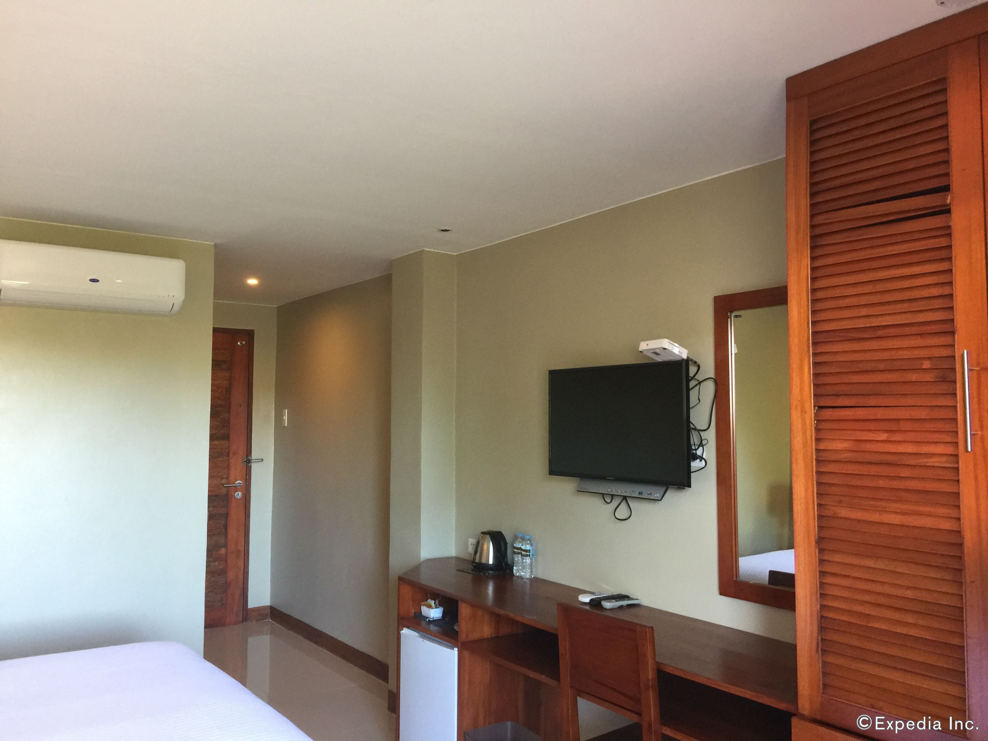 A hotel room with a bed, a desk with a computer, a television, a wardrobe, and an air conditioning unit.