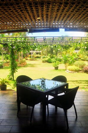 A covered patio with a table and chairs, surrounded by lush greenery and a view of a building in the background. - Golden Palm Resort (Panglao)