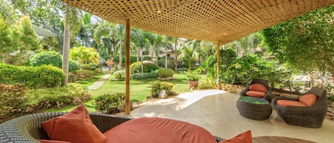 Un espacio de estar al aire libre techado, con mobiliario de mimbre y vistas a un jardín cuidado.