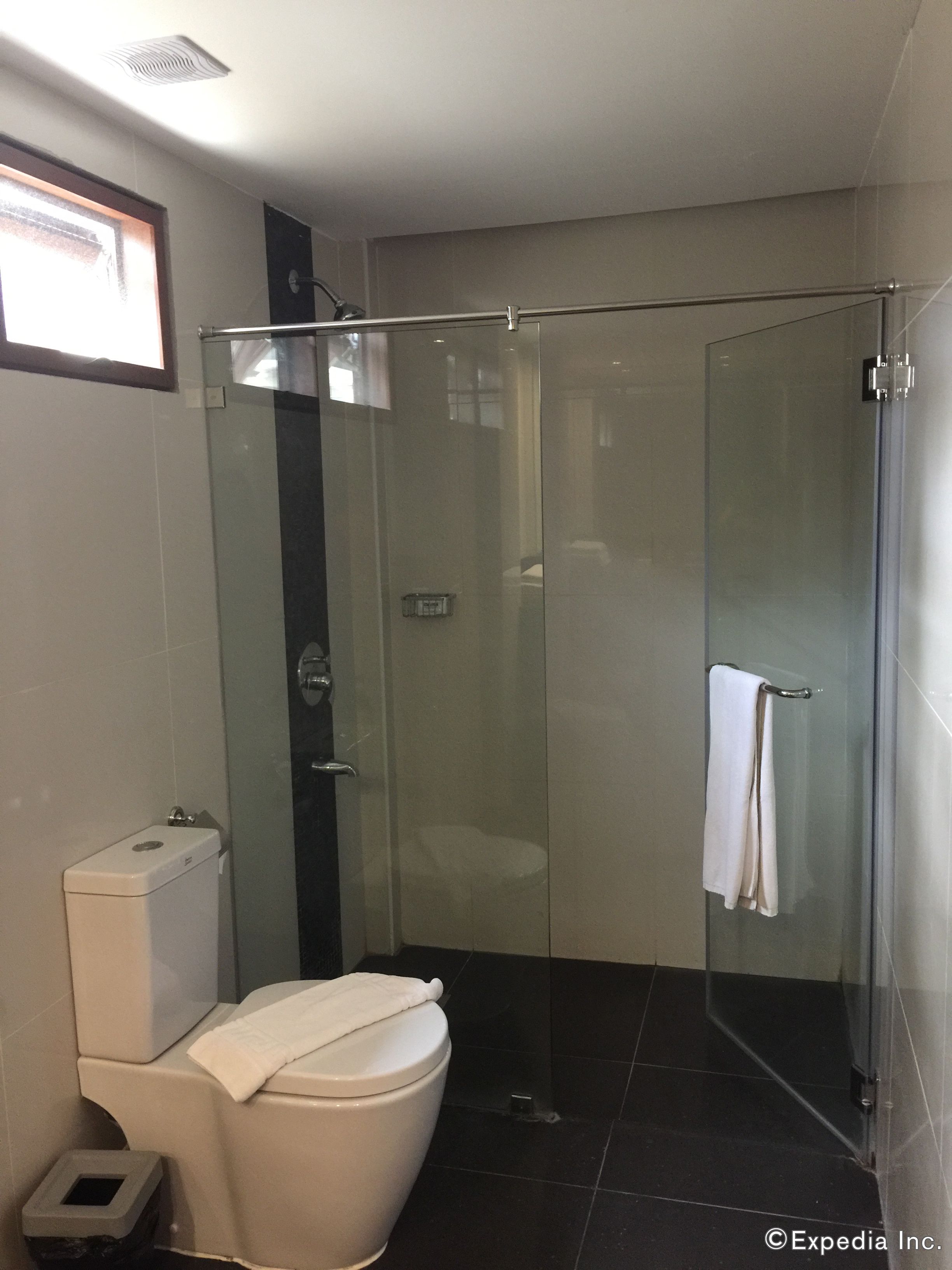 A modern bathroom with a glass-enclosed shower, a toilet, and a small trash bin.
