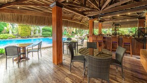 An outdoor bar area with wooden flooring, wicker furniture, and a pool in the background.