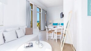 A modern, well-lit room with a white sofa, a dining table with chairs, and a painting on the wall. - Aqua Marina (Rethymno)