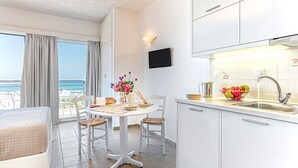 A modern kitchen with white cabinets, a dining table with chairs, a view of the ocean through large windows, and a flat-screen TV mounted on the wall. - Aqua Marina (Rethymno)