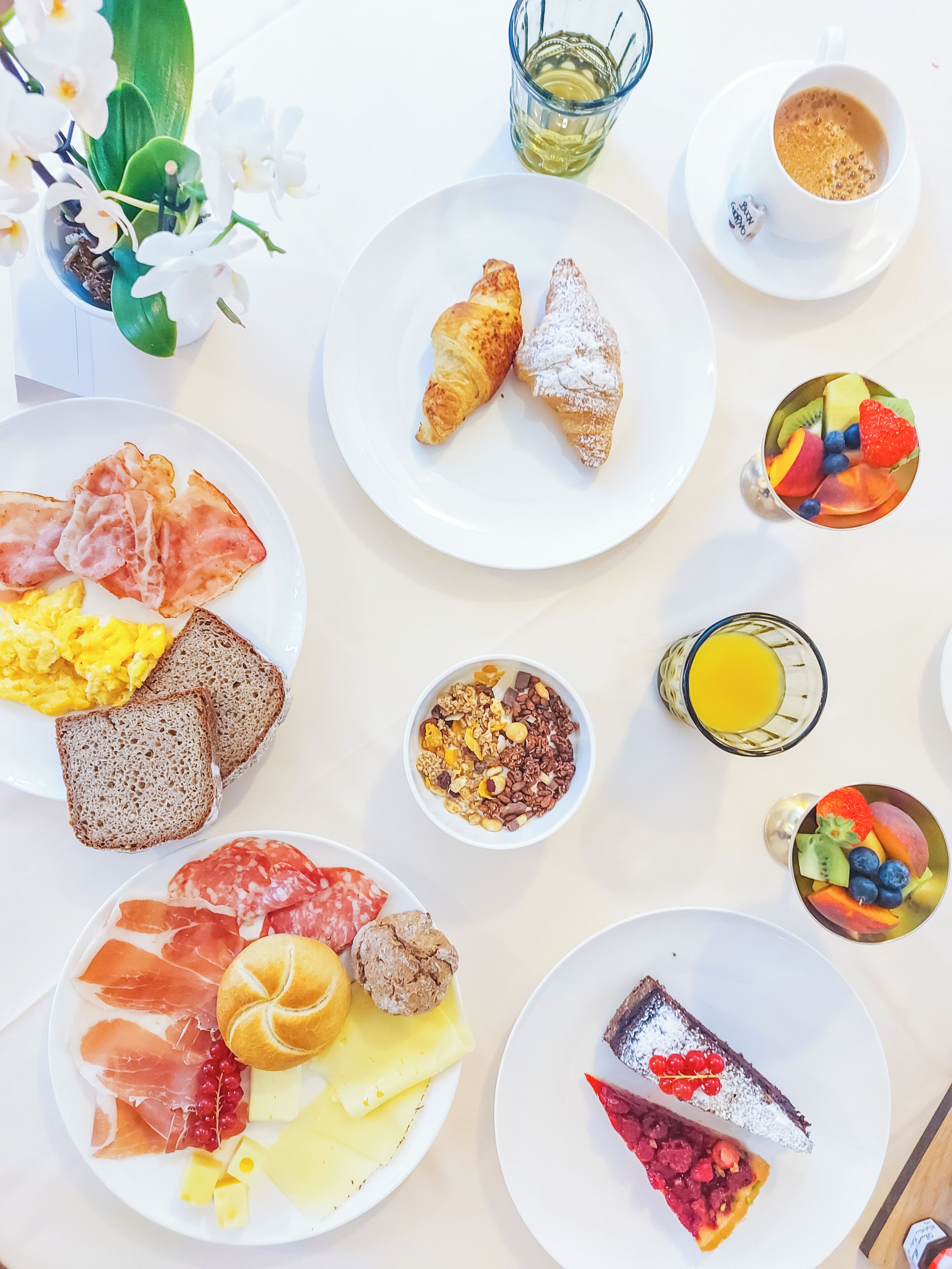 A breakfast spread with croissants, scrambled eggs, smoked salmon, cheese, and fruit.