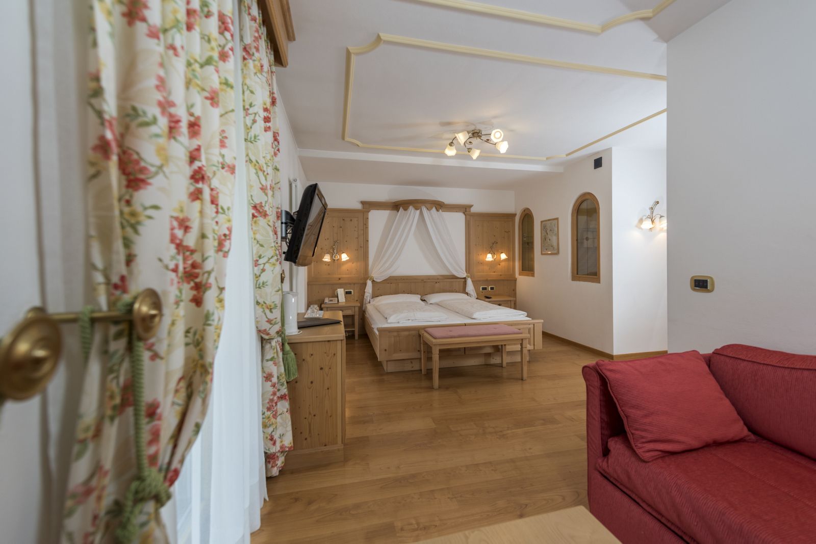 A bedroom with a wooden bed, a bedside table, a red sofa, and a ceiling light fixture.